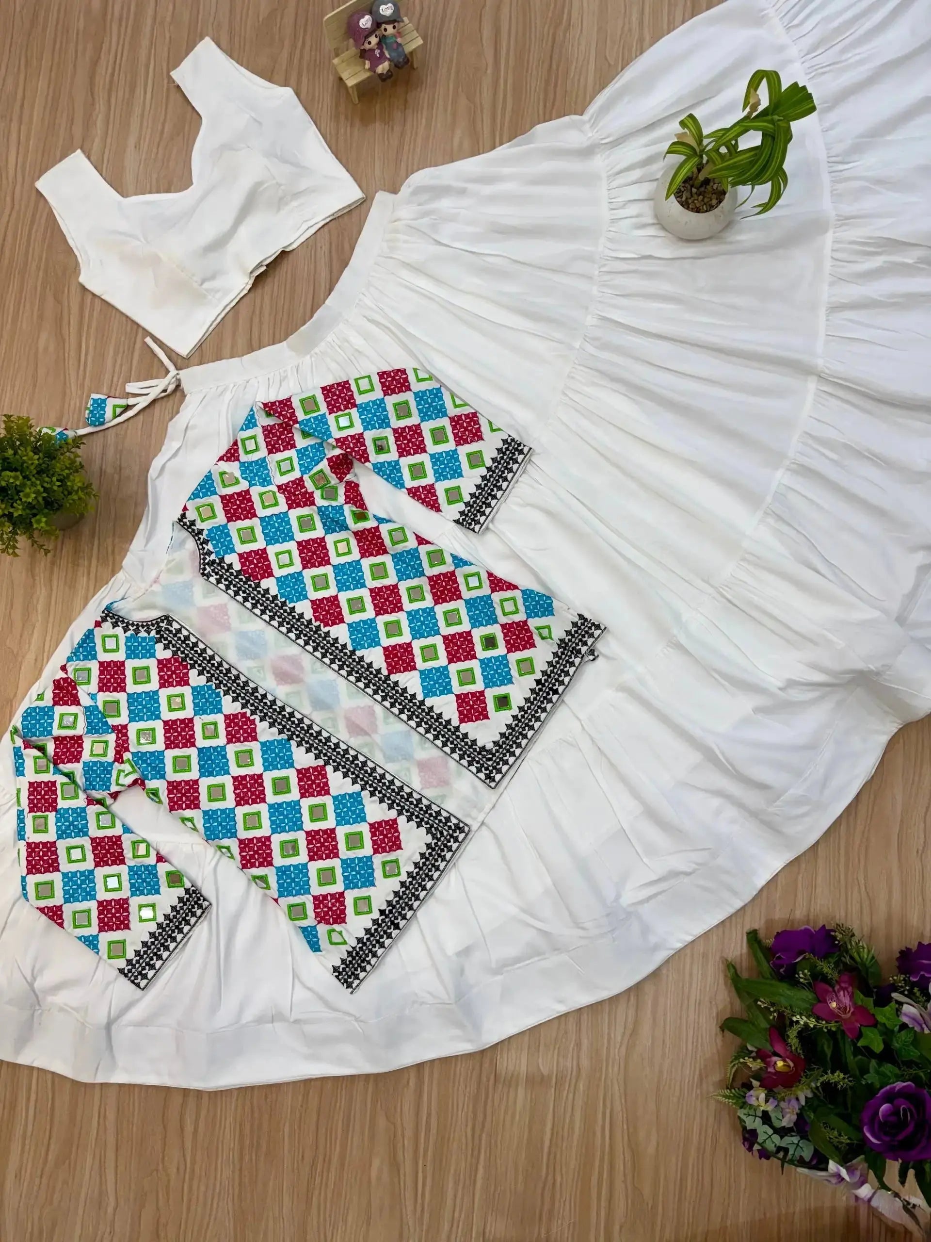 Flat lay of white lehenga set showing bandhej jacket, white choli and tiered skirt detail
