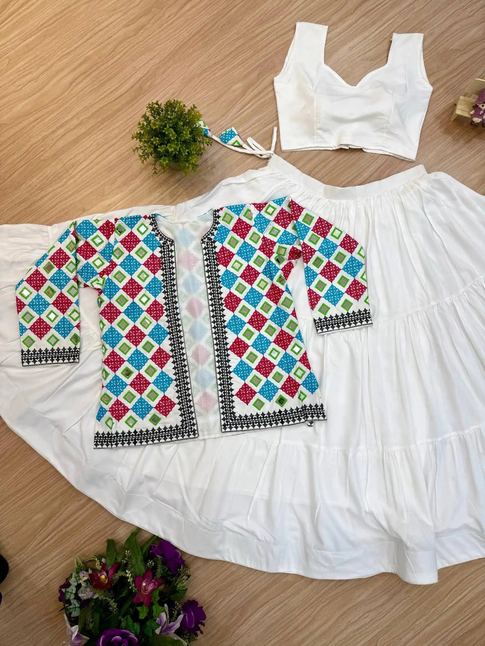 Flat lay of full white mirror work lehenga set with bandhej koti, inner choli and tiered skirt