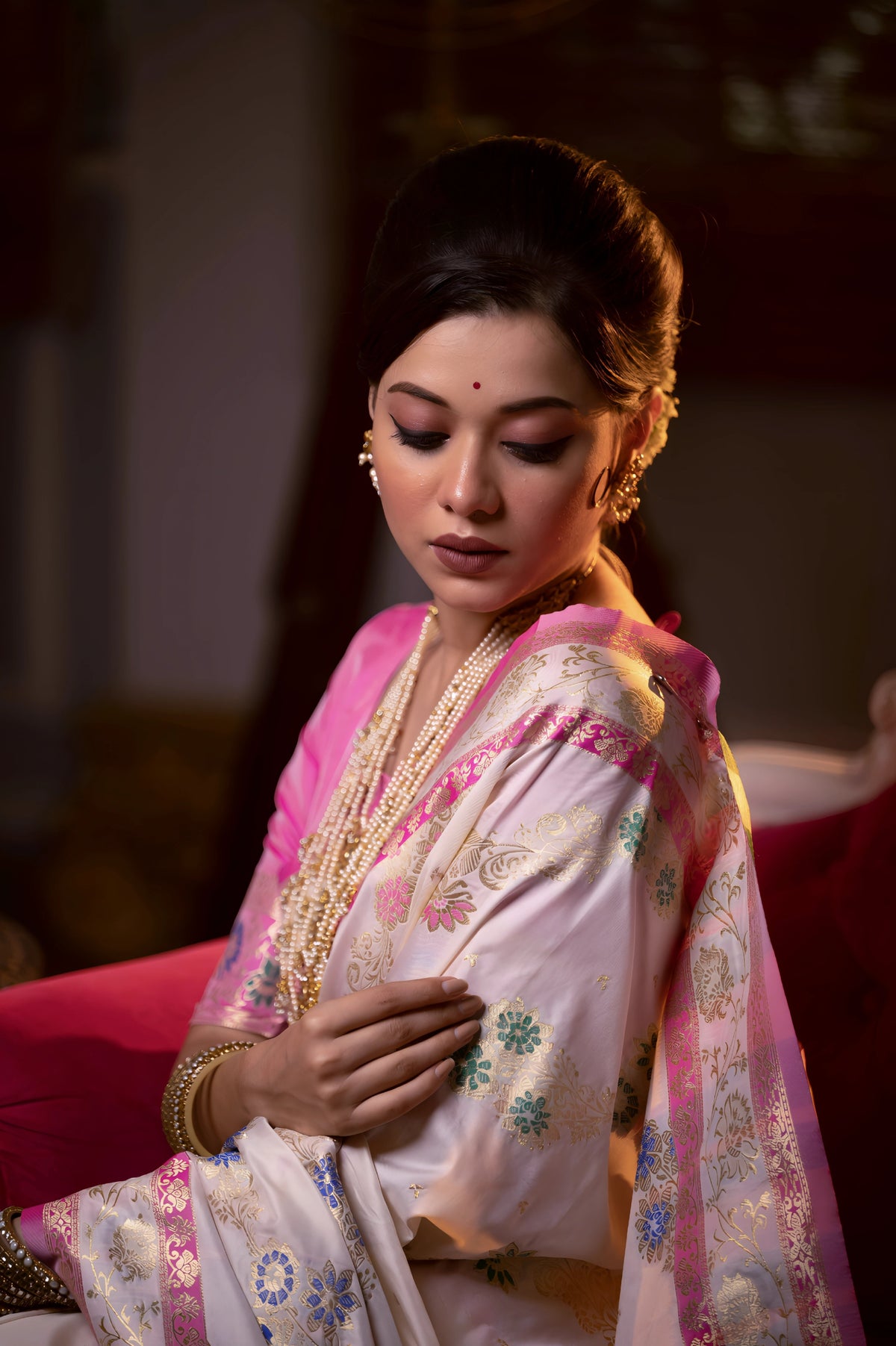 A woman models an opulent Off-White Soft Banarasi Silk Saree. The saree features multi-colored motifs and a wide Fuchsia Pink and gold Zari woven border and pallu with traditional patterns. She wears a contrasting pink long-sleeve blouse and heavy layered gold and pearl jewelry, posing in a luxurious, dramatically lit vintage setting.
Related
File name: modern-minimalist-architecture
Alt text: Sleek modern minimalist architecture with clean lines and large glass windows
