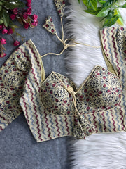 Beige padded blouse with maroon and navy geometric and floral patterns, displayed on a white fur surface with artificial flowers and green leaves in the background.Beige padded blouse with maroon and navy geometric and floral patterns, displayed on a white fur surface with artificial flowers and green leaves in the background.
