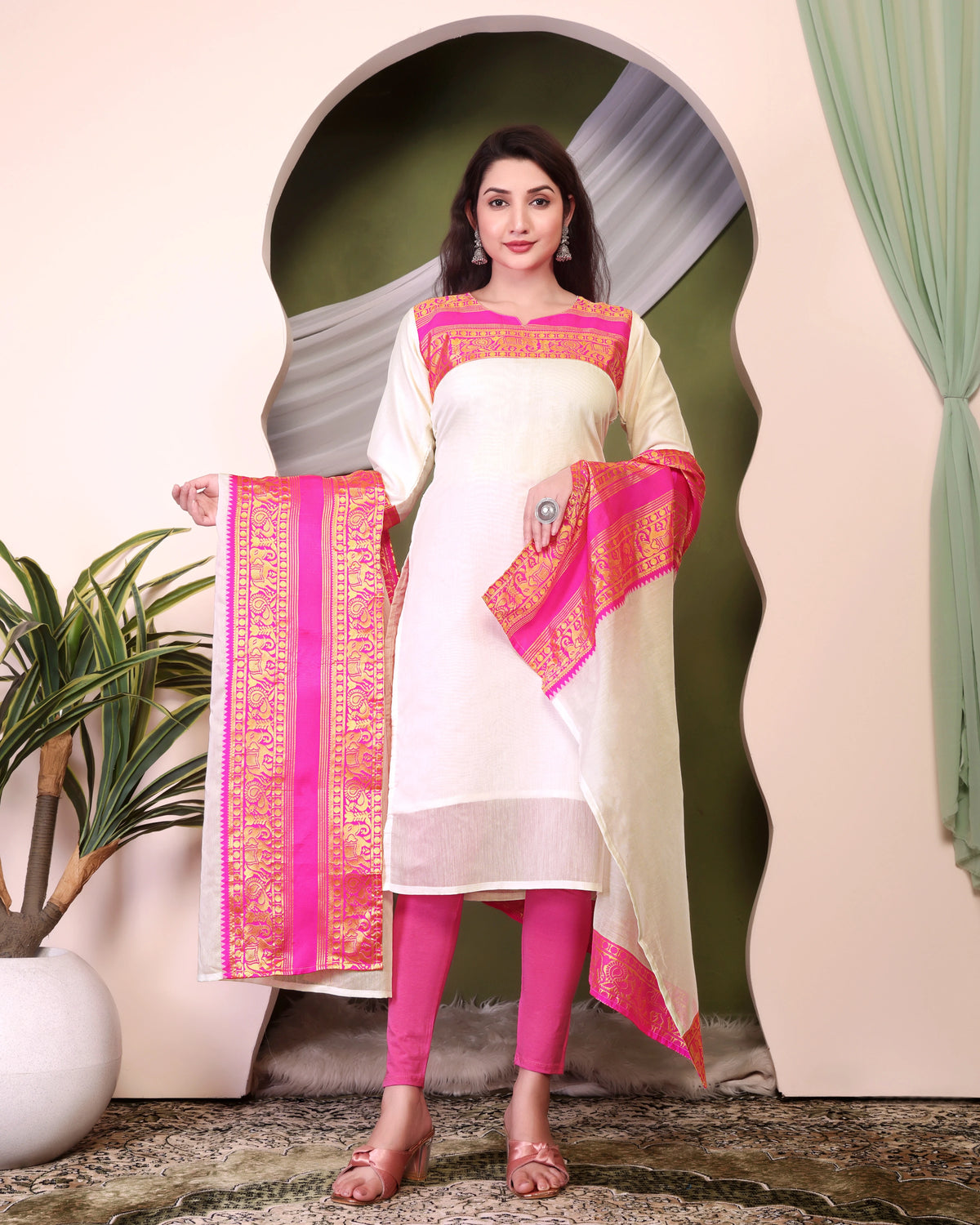 Woman in a white and pink traditional outfit with a decorative scarf, standing indoors.