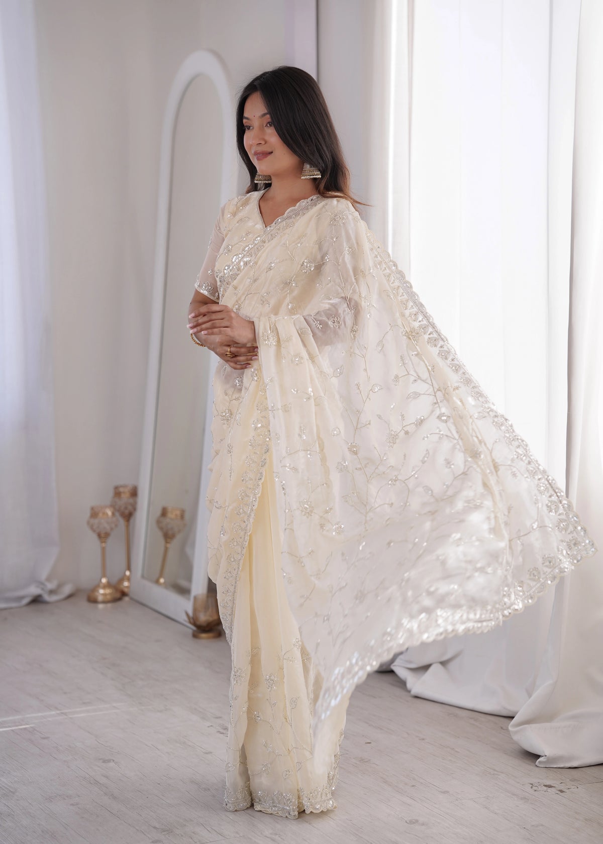 Woman in a white embroidered saree standing in a softly lit room.