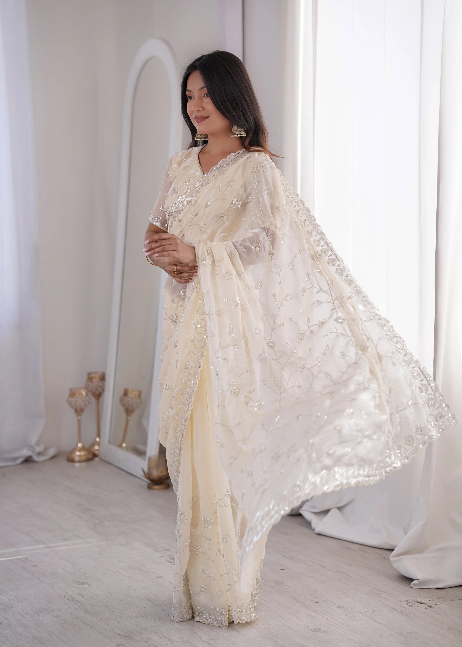 Woman in a white embroidered saree standing in a softly lit room.