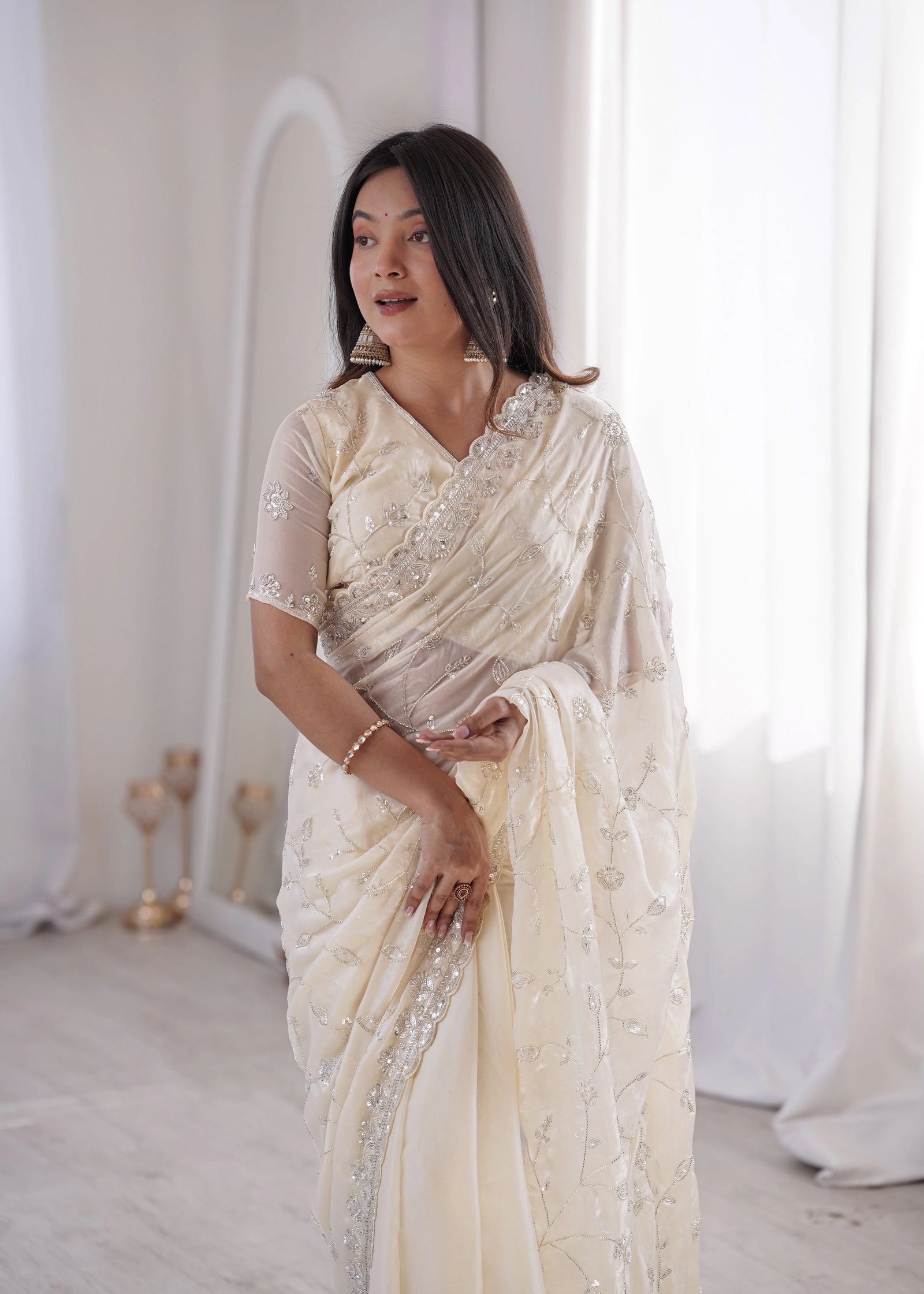 Woman in a white saree with intricate designs in a minimalistic setting