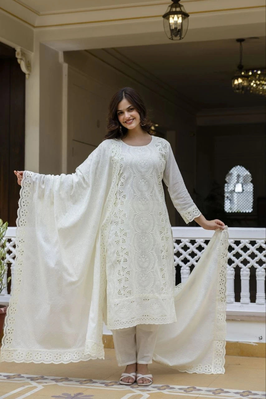 Woman in a white embroidered outfit holding a matching dupatta in an elegant indoor setting.