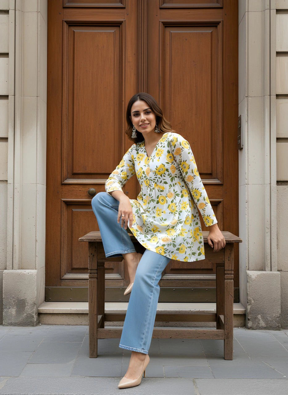 Woman sitting on a wooden bench in front of a large wooden door wearing a floral dress and jeans.