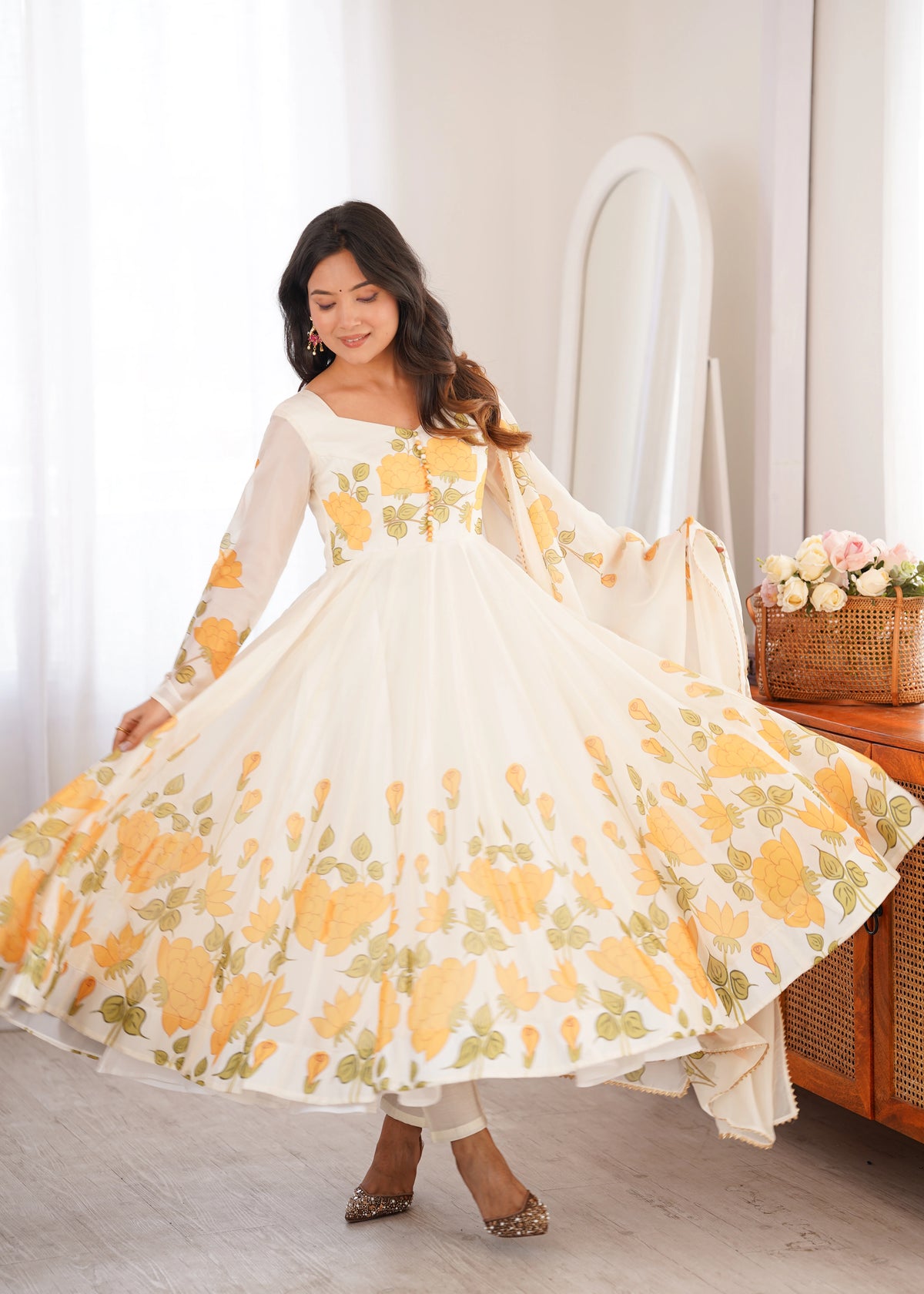 Woman wearing a white dress with yellow floral patterns in a room.