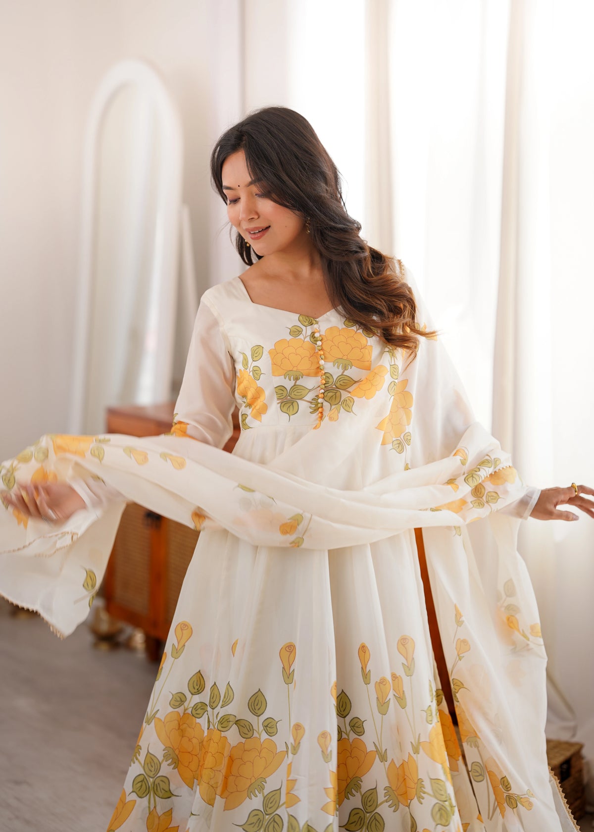 Woman wearing a white dress with yellow floral patterns in a softly lit room.