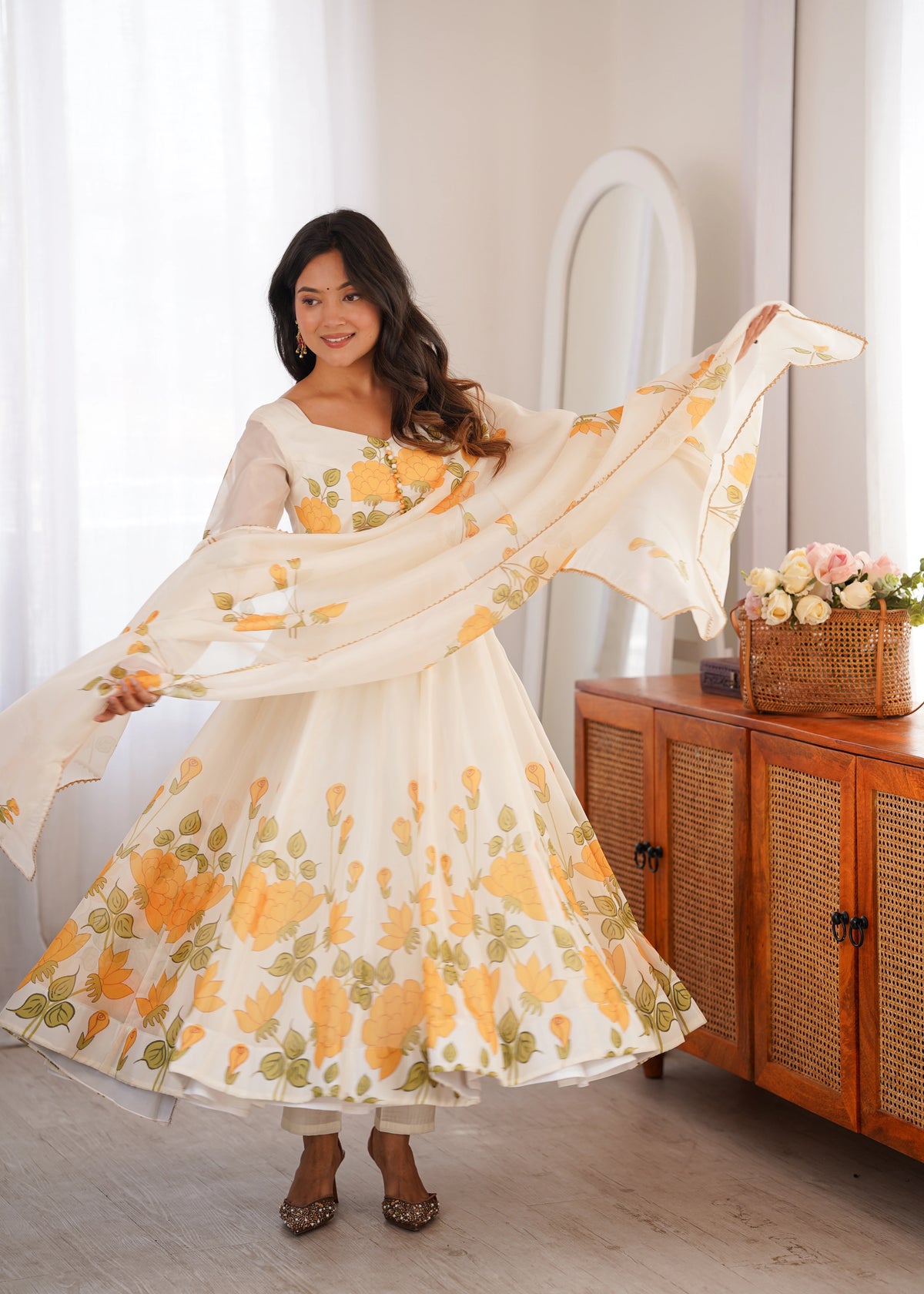 Woman in a floral dress holding a matching shawl in a bright room.