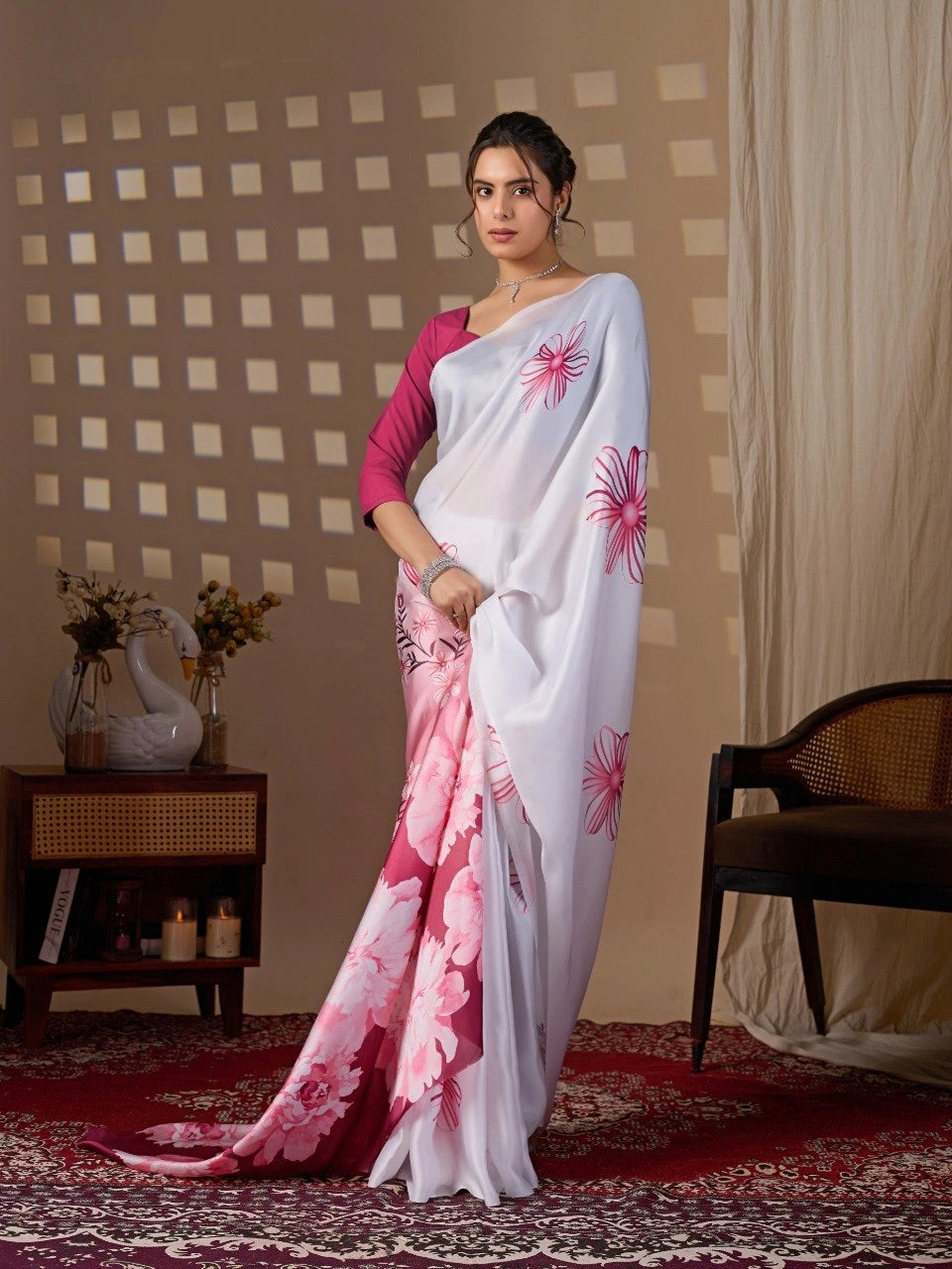 Woman wearing a white saree with pink floral patterns in a room setting.