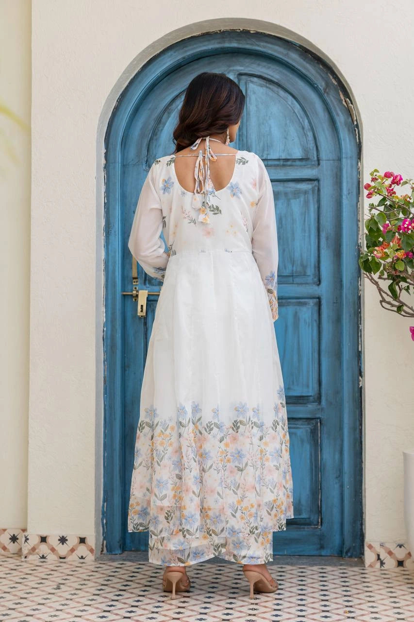 Woman in a floral dress standing in front of a blue door with a white wall and decorative elements.