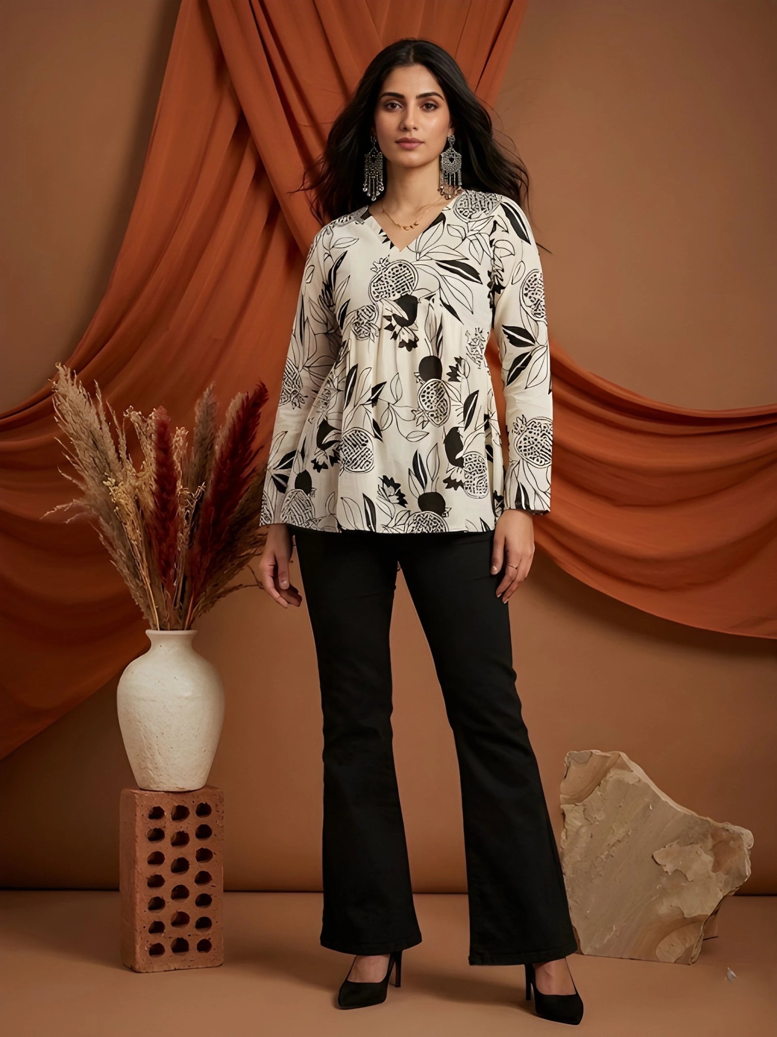 Woman wearing a black and white patterned top with black pants against a brown curtain background.
