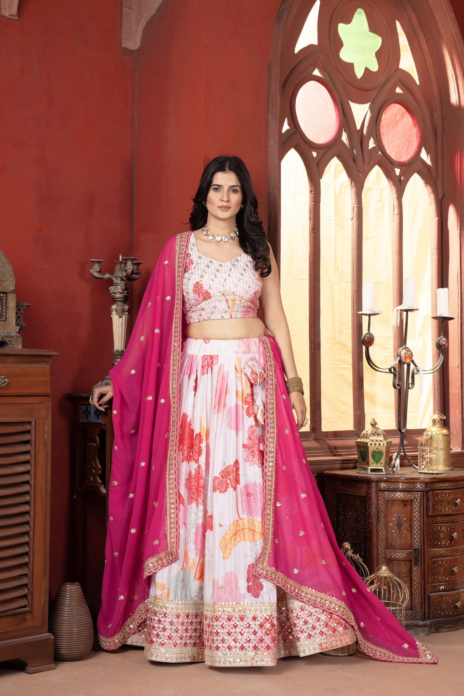Woman in a floral lehenga with a pink dupatta standing in a decorated room.