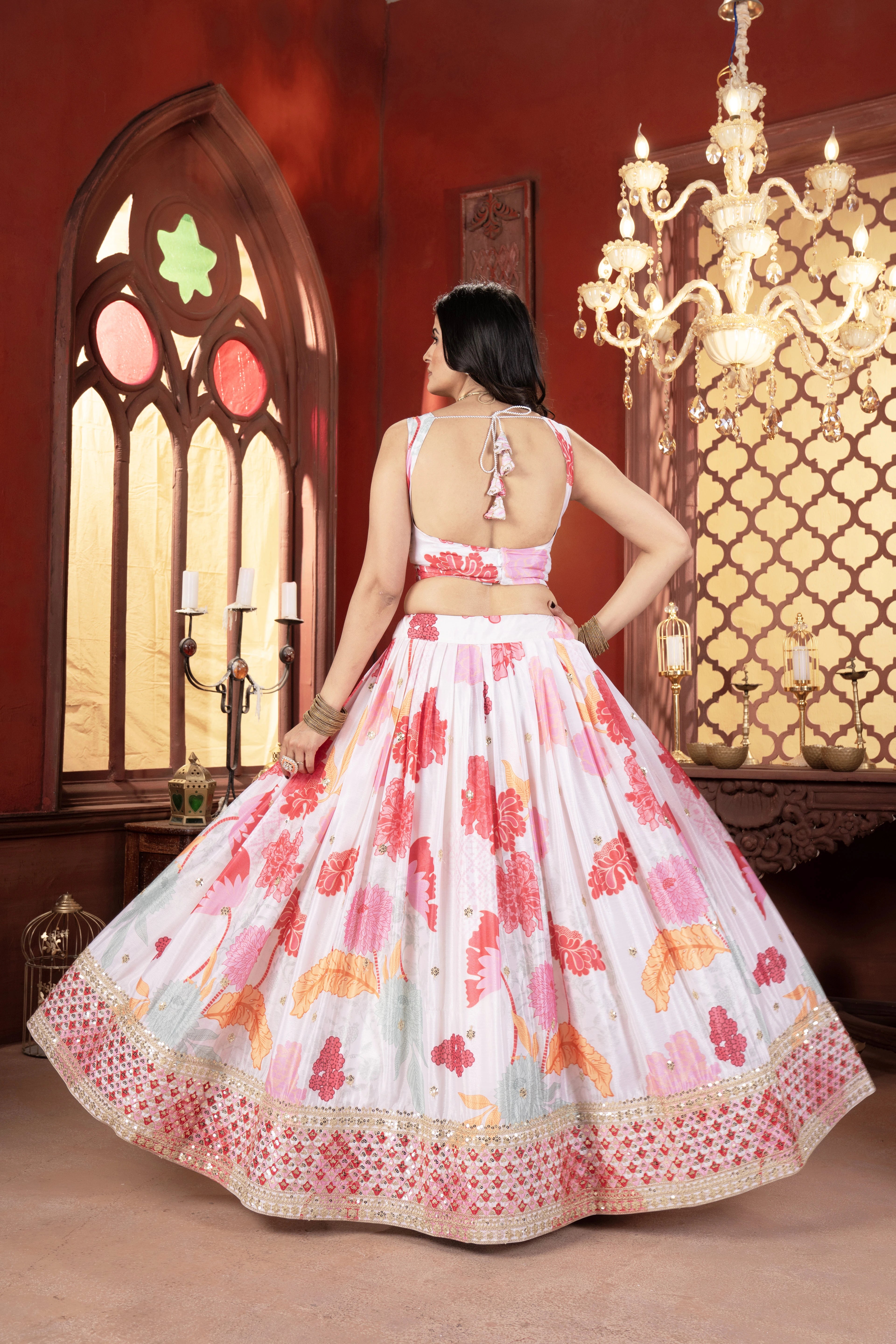 Woman in a floral dress standing in a room with a chandelier and stained glass window.