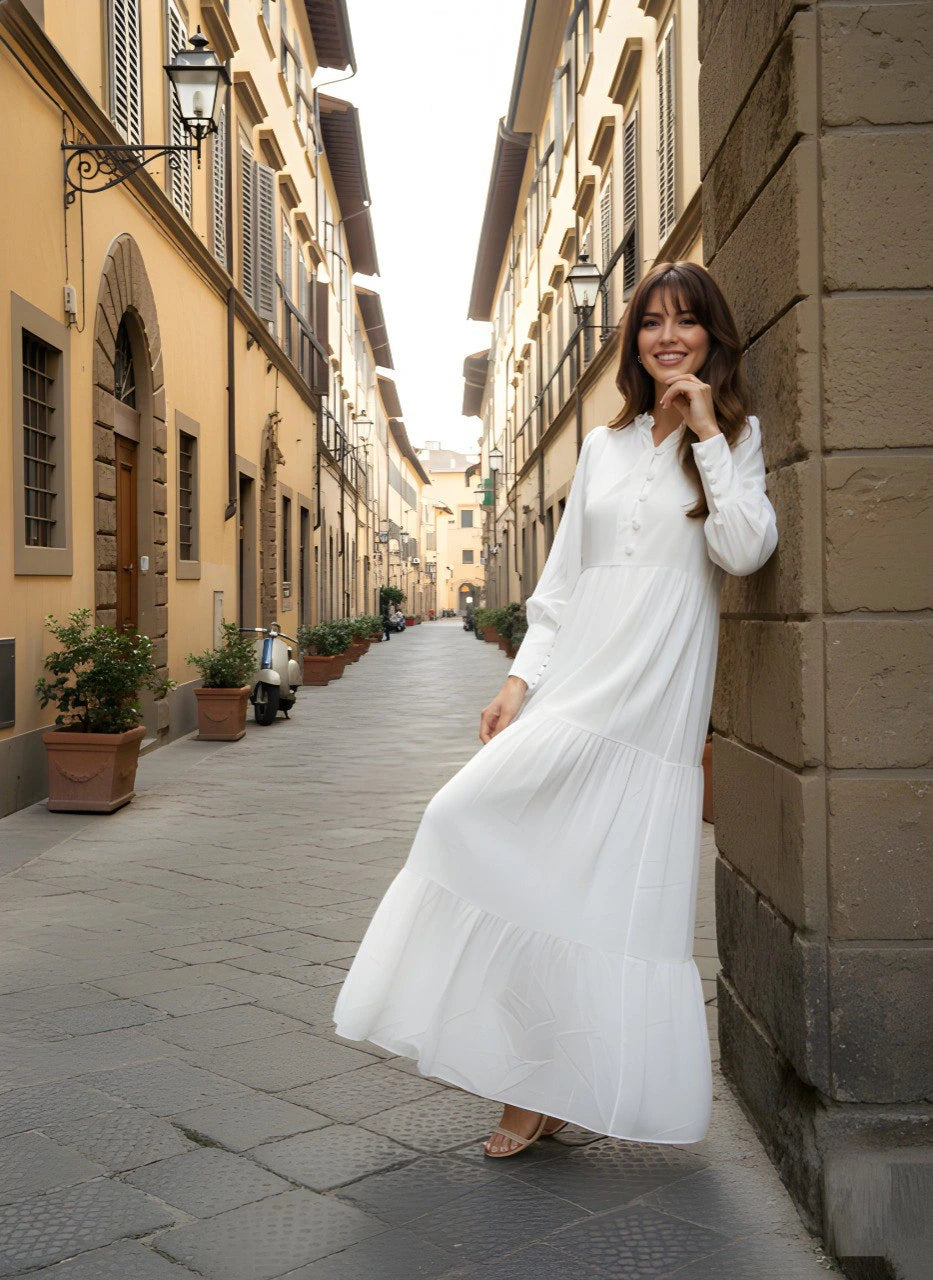 Woman in a white dress standing on a narrow street with buildings on either side.