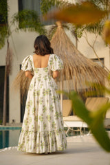 Woman in a floral dress standing by a poolside with a thatched umbrella in the background