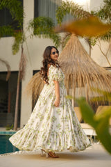 Woman in a floral dress standing by a pool with a thatched roof structure in the background.