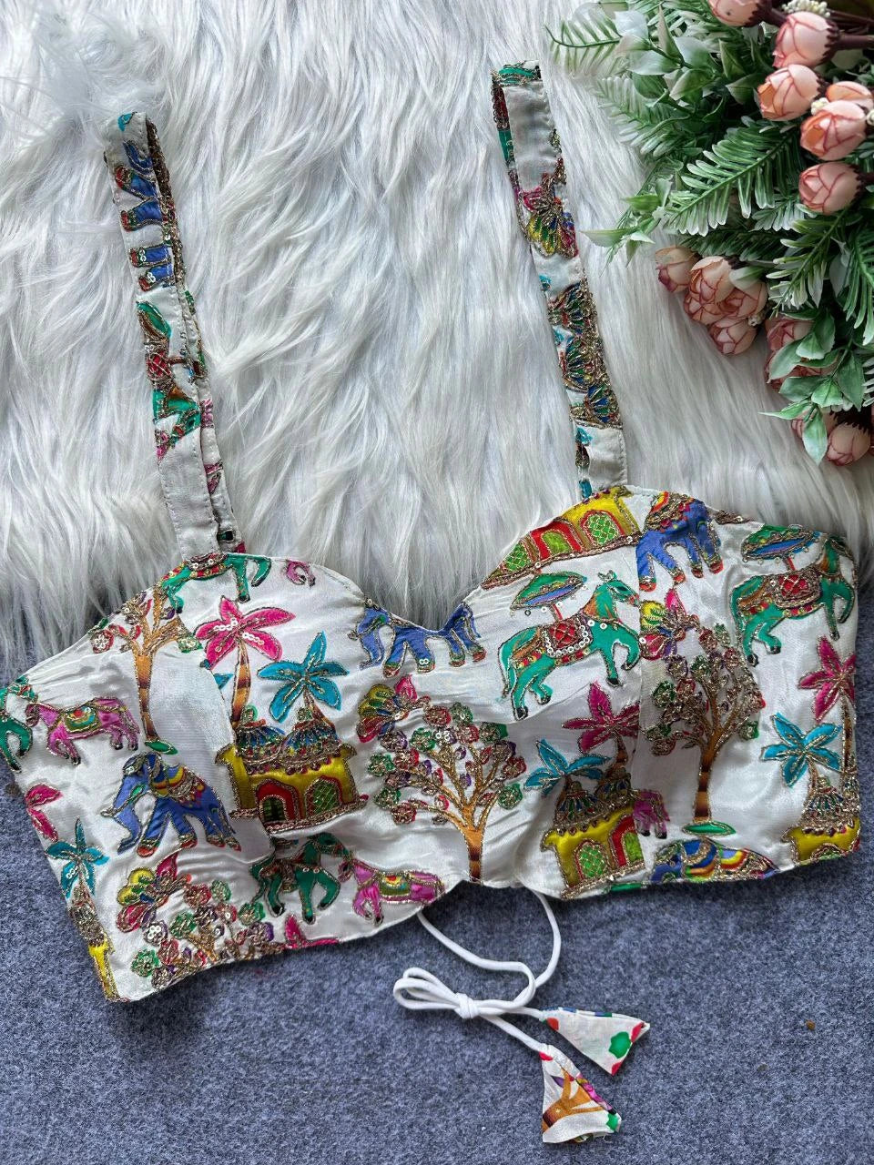 Colorful embroidered bralette with floral and elephant patterns on a textured surface.