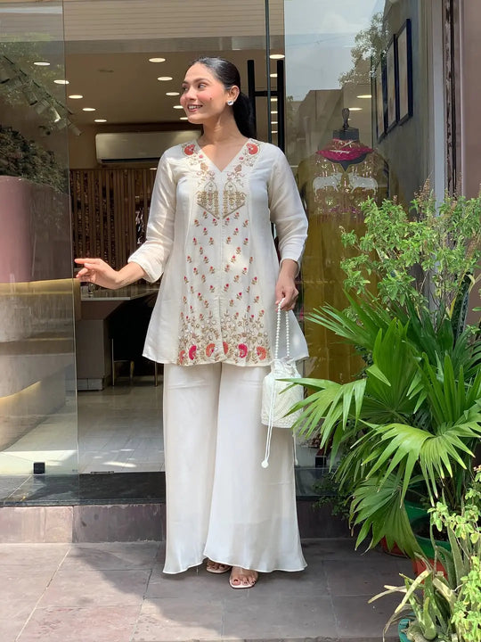 Woman in a white traditional outfit standing in front of a store entrance.