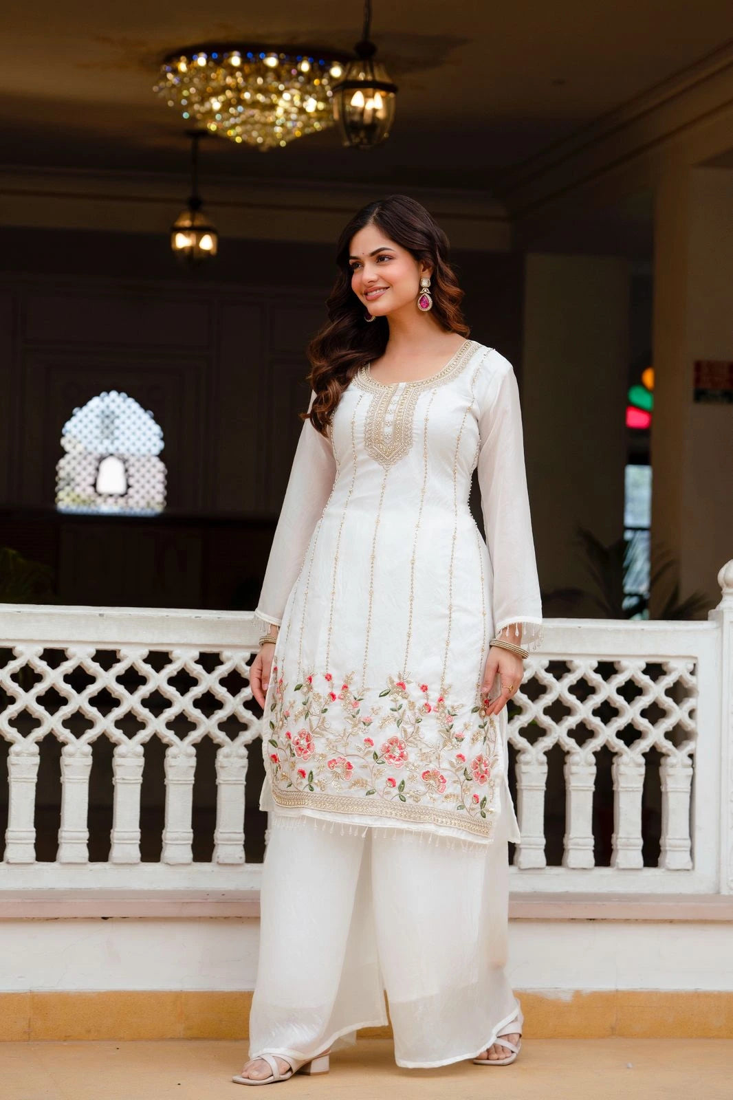 Woman in a white traditional outfit with floral details standing indoors.
