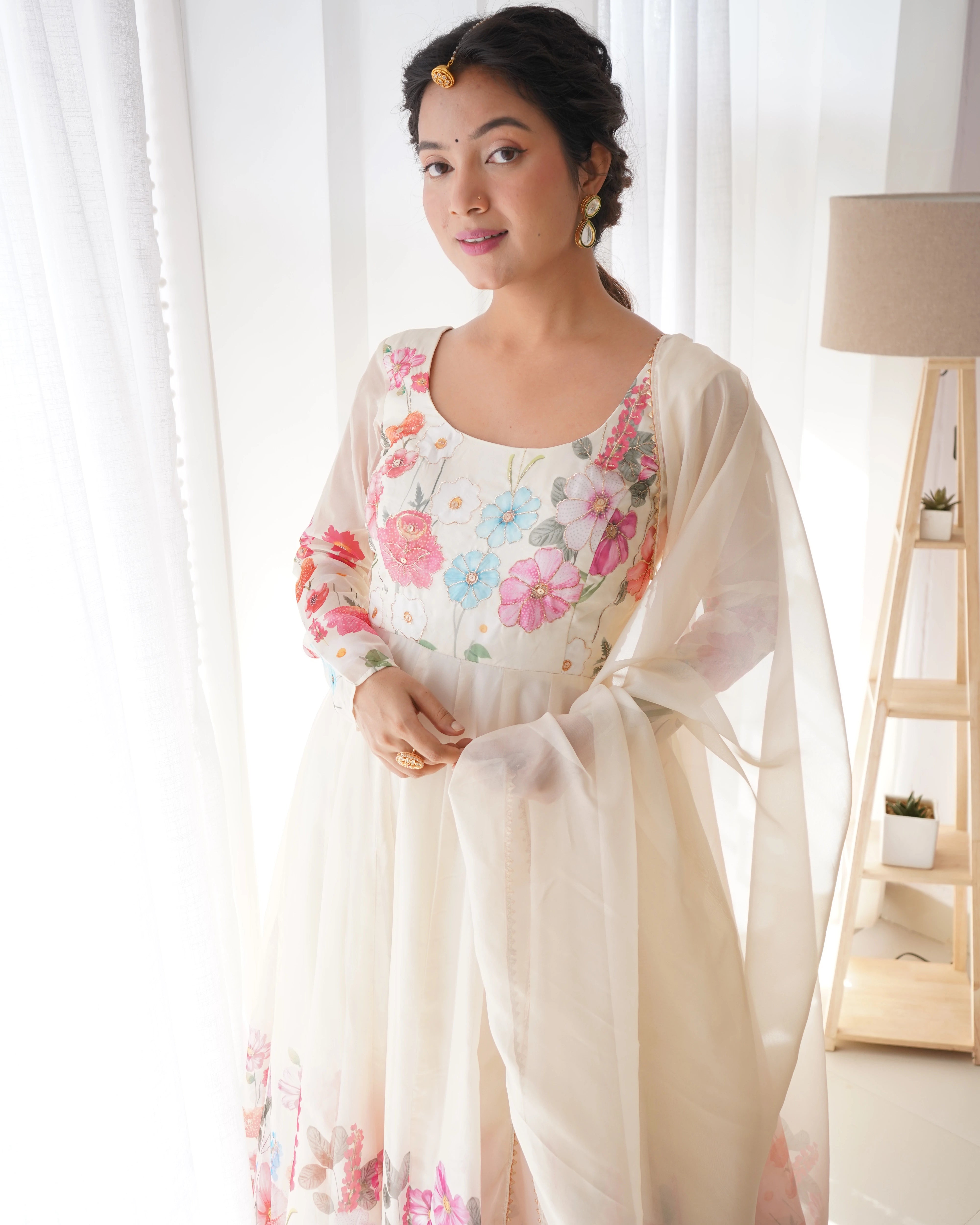 Woman wearing a floral dress with a sheer dupatta in a bright room.