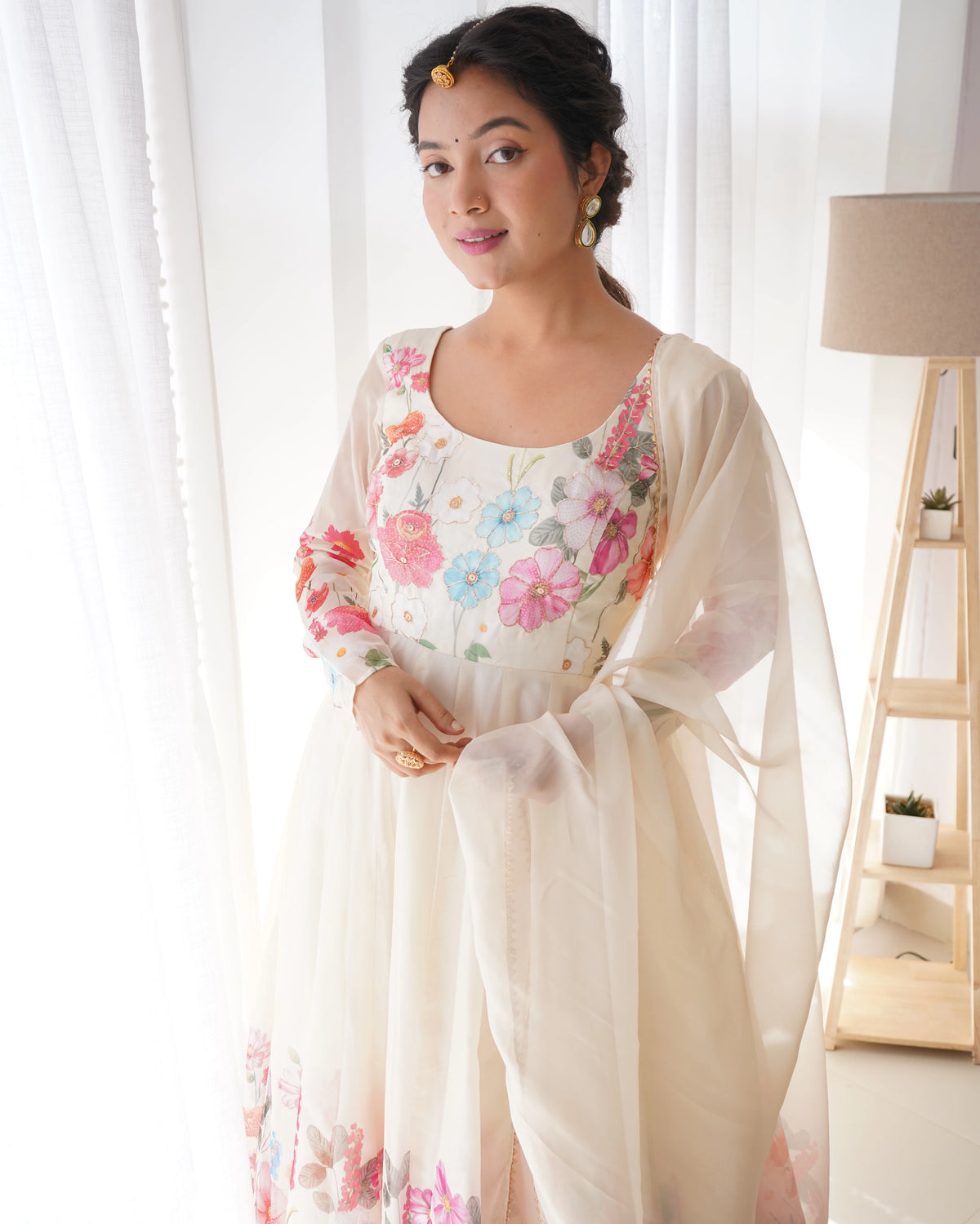 Woman wearing a floral dress with a sheer dupatta in a bright room.