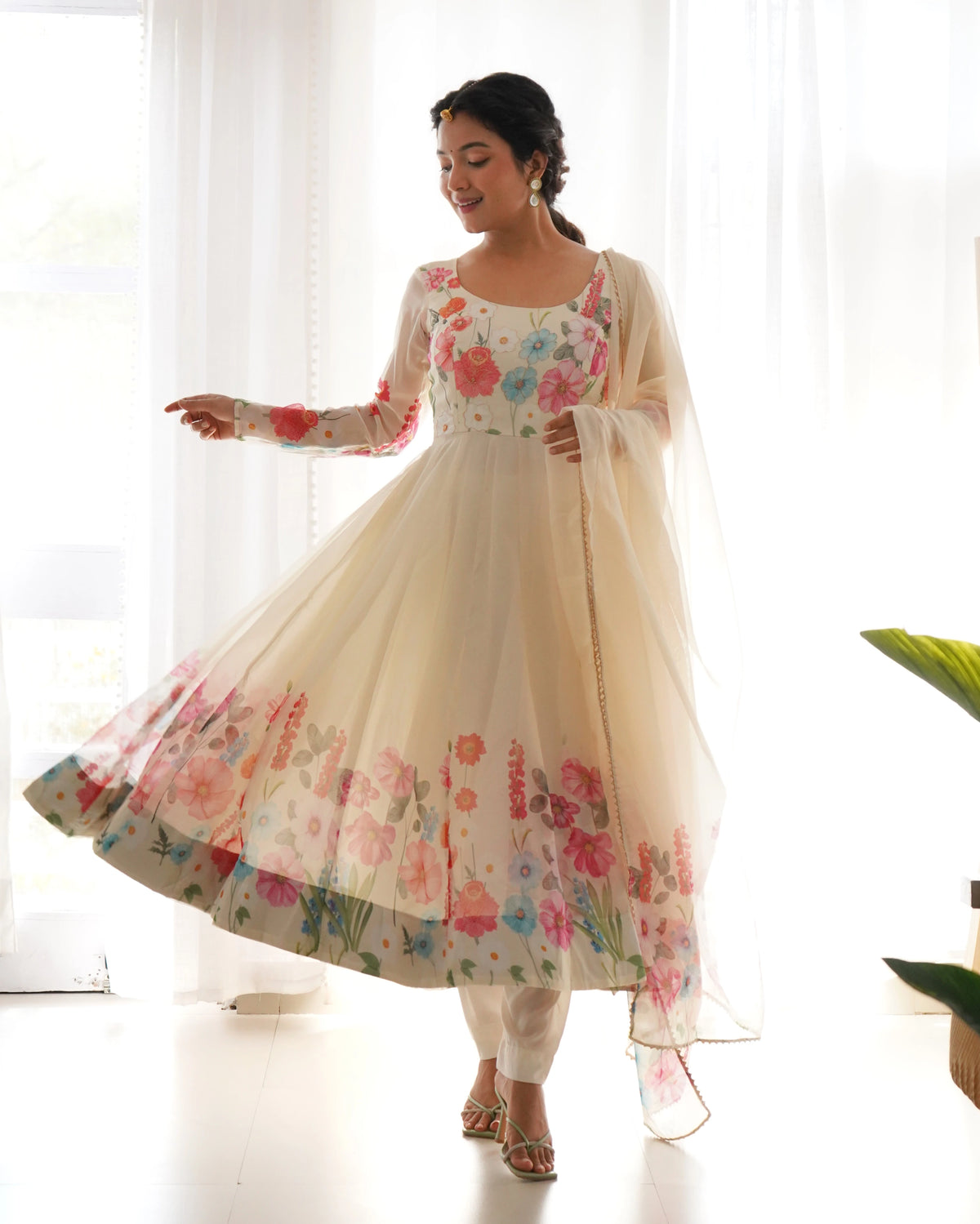 Woman wearing a floral dress with a sheer dupatta against a white curtain background