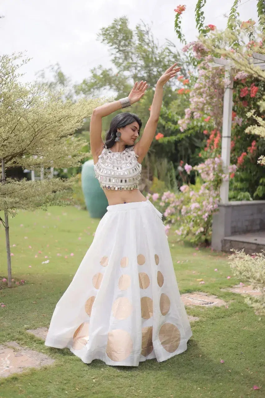 Elegant white lehenga choli featuring a sleeveless mirror work blouse and a flared skirt with bold golden polka dot motifs.