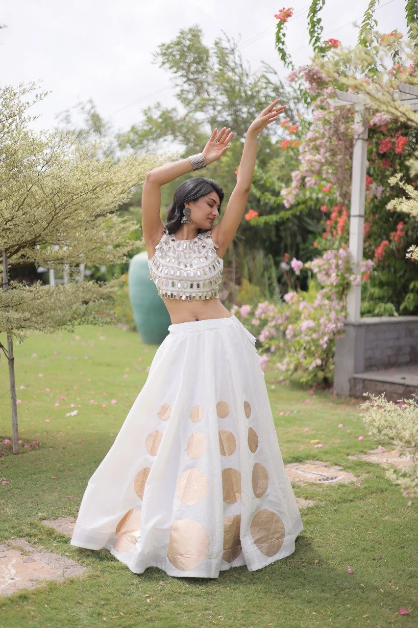 Elegant white lehenga choli featuring a sleeveless mirror work blouse and a flared skirt with bold golden polka dot motifs.