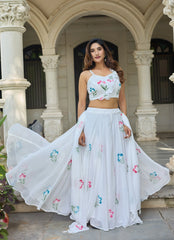 Woman in a white embroidered outfit standing in front of an architectural building.