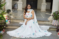 Woman in a white embroidered saree sitting on steps outdoors.
