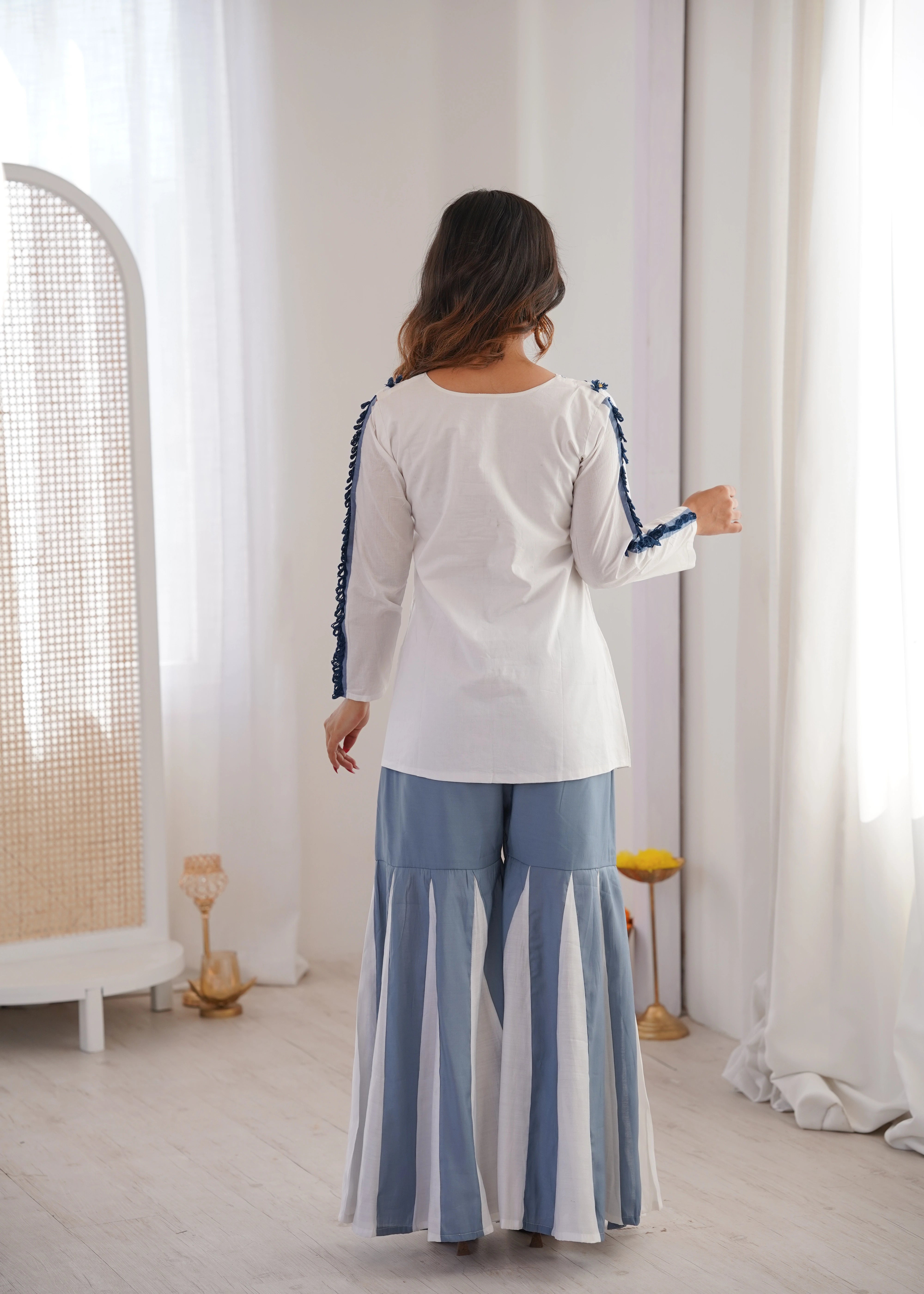 Woman wearing a white top with blue trim and striped pants in a bright room.