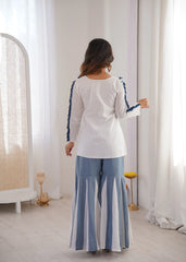 Woman wearing a white top with blue trim and striped pants in a bright room.