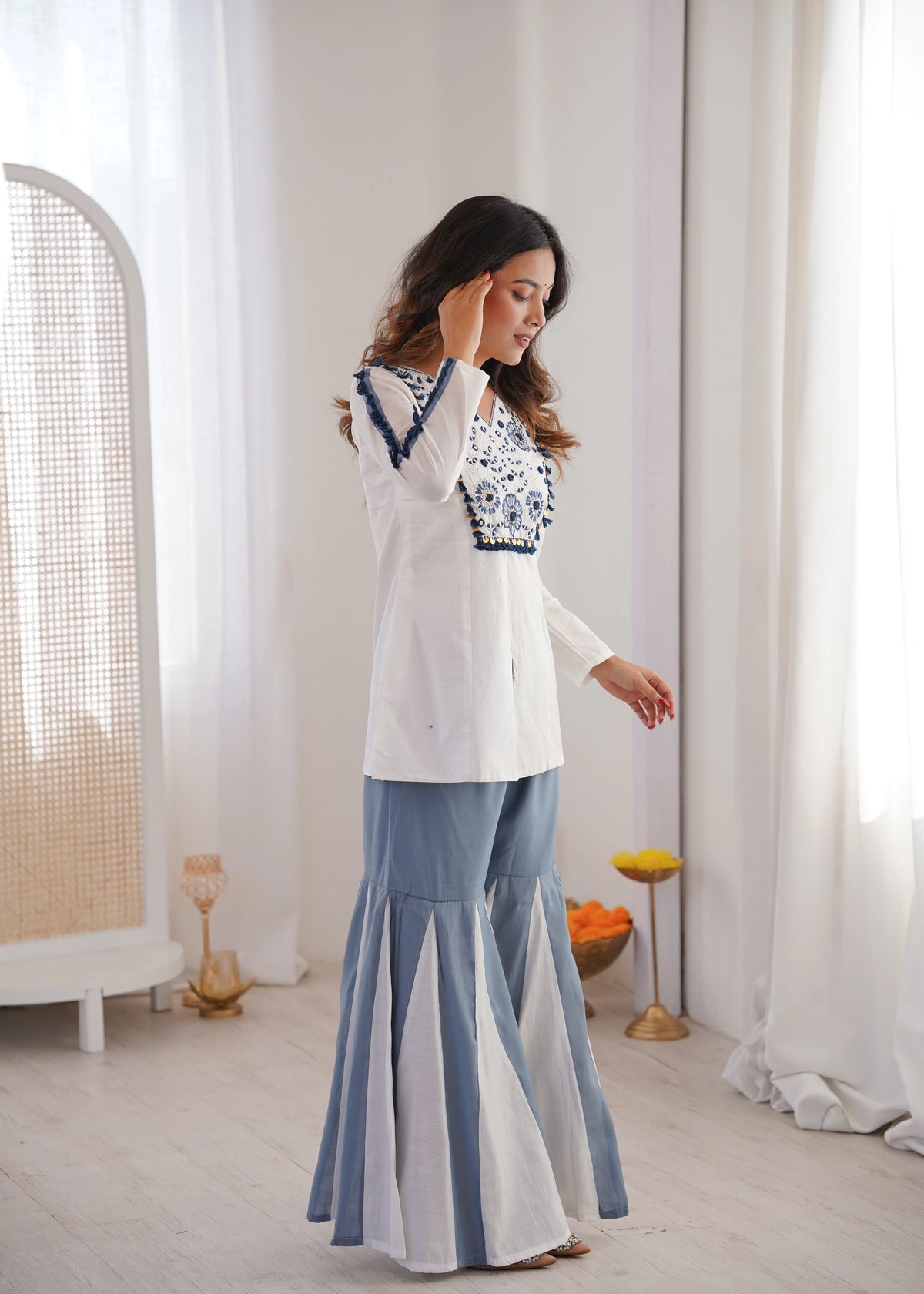 Woman wearing a white and blue outfit in a minimalistic room.