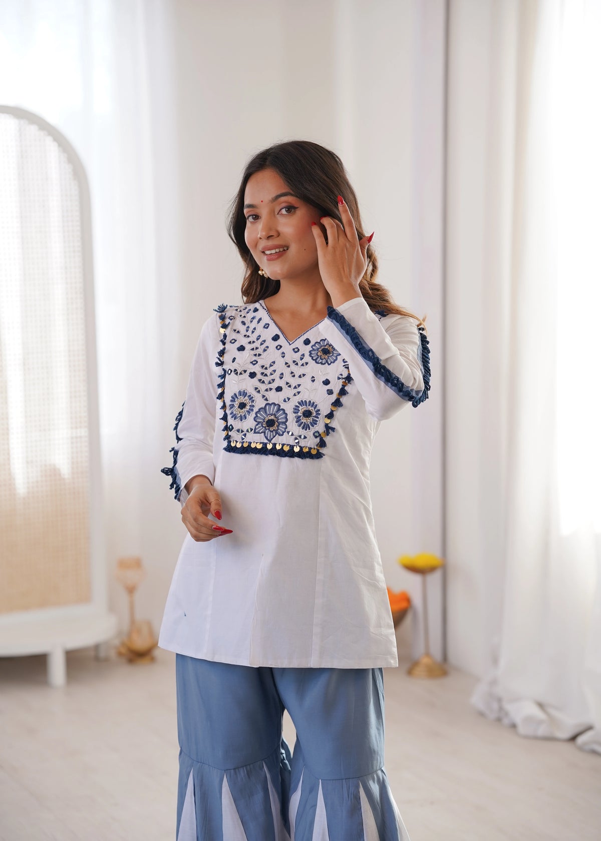 Woman wearing a white top with blue embroidery in a bright room.