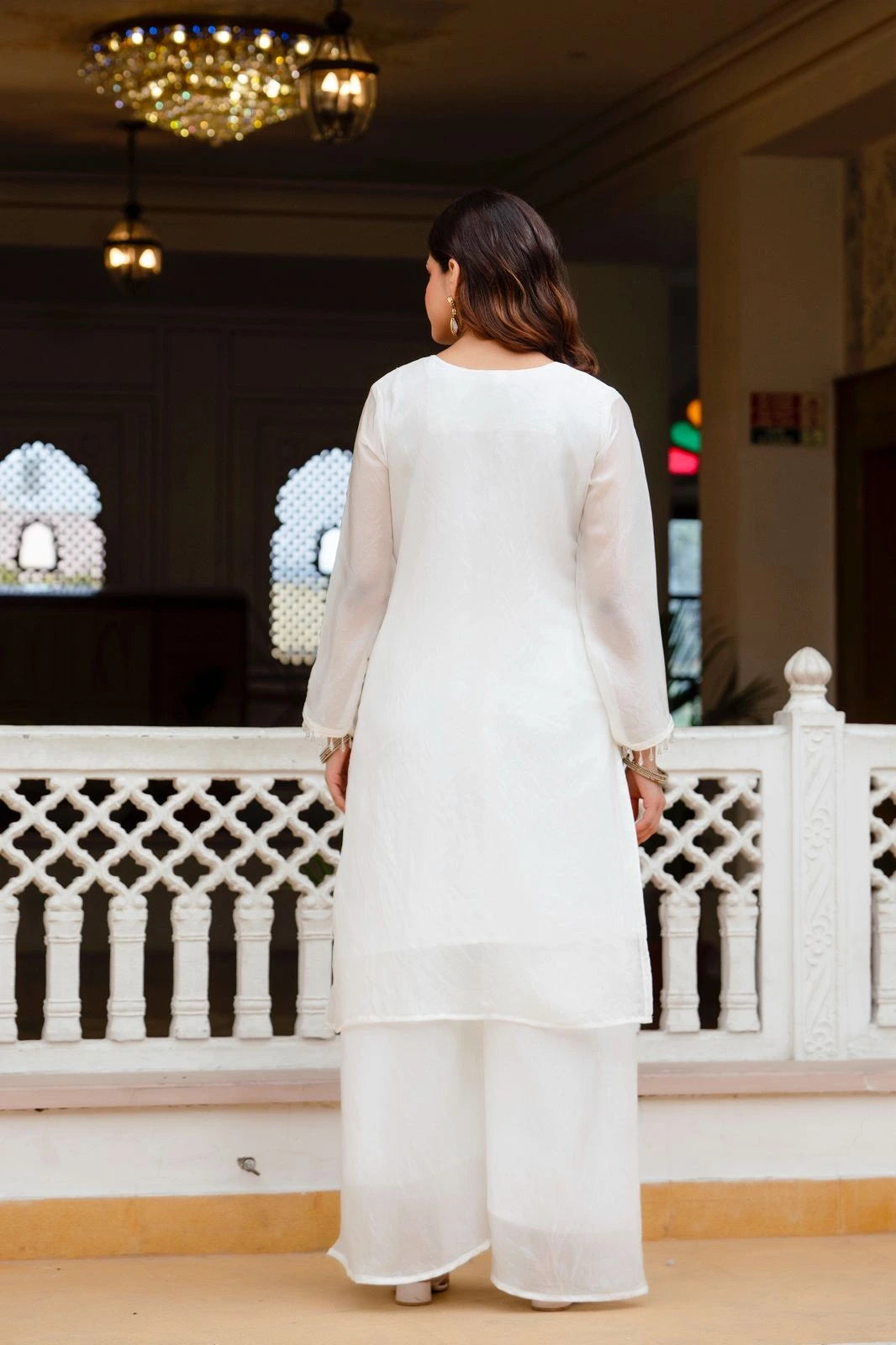 Woman in a white outfit standing on a balcony with decorative railings.