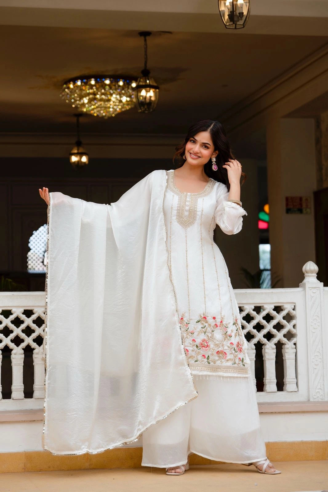 Woman in a white traditional outfit with floral embroidery in an indoor setting.