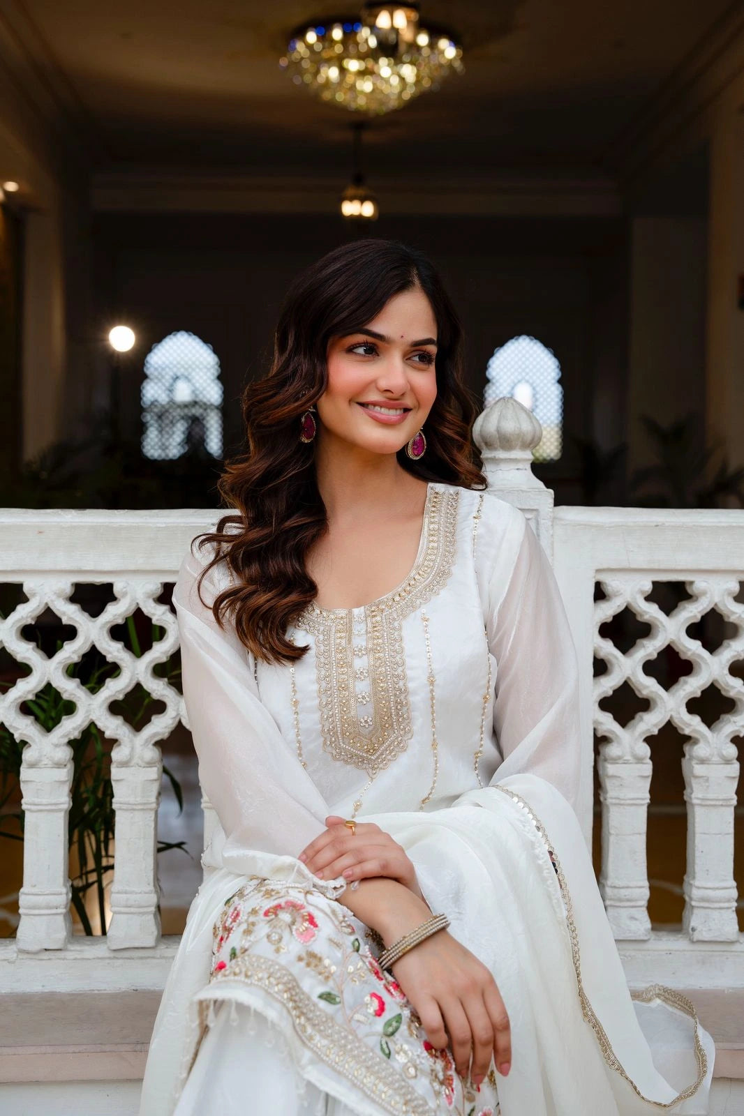 Woman in a white traditional outfit sitting on a decorative balcony.