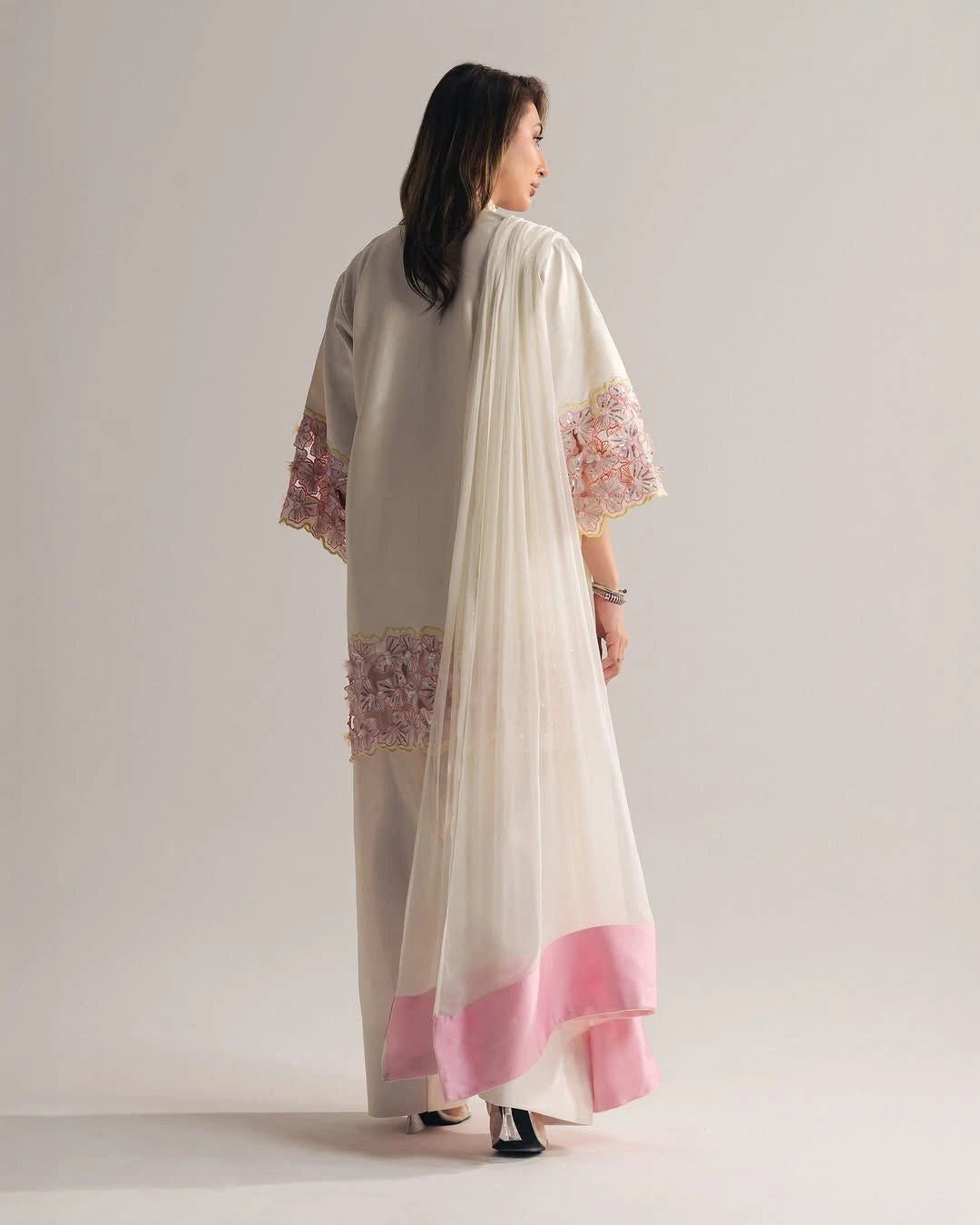 Woman wearing a cream and pink traditional outfit with floral embroidery on a plain background