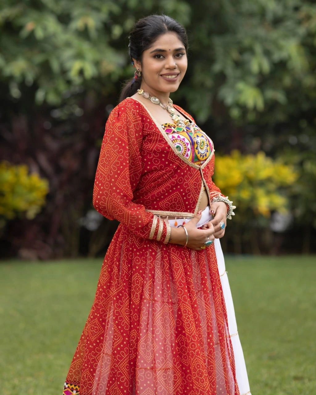 Woman in a red traditional outfit with intricate patterns standing outdoors.