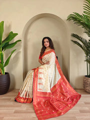 Woman in a white and red saree standing indoors with plants on either side.