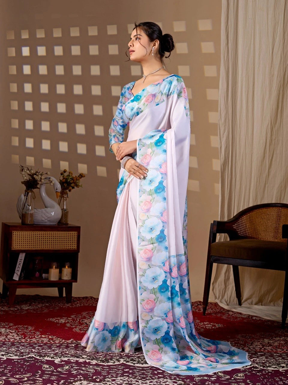 Woman in a floral saree standing in a room with a checkered wall and a chair.
