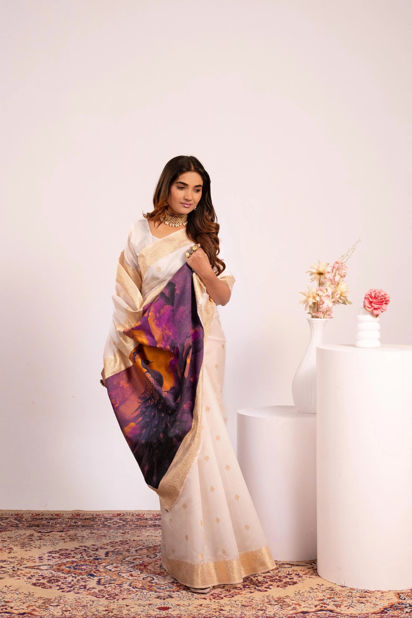 Woman wearing a cream saree with a colorful pattern, standing against a white background.