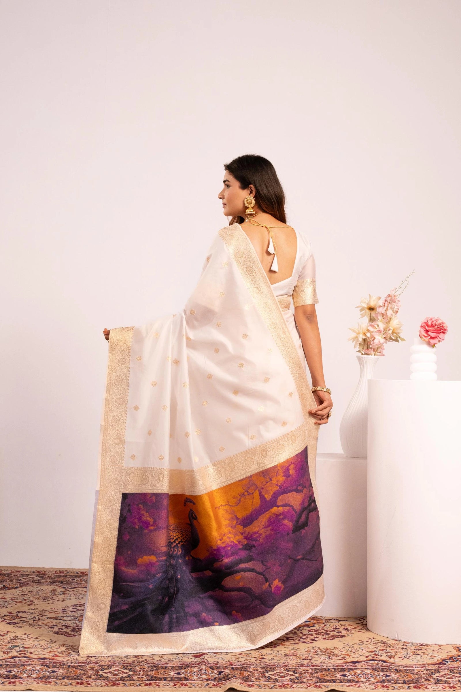 Woman holding a white saree with a colorful design on a plain background