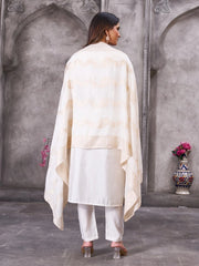 Woman wearing a cream-colored outfit with a long drape against a gray wall.