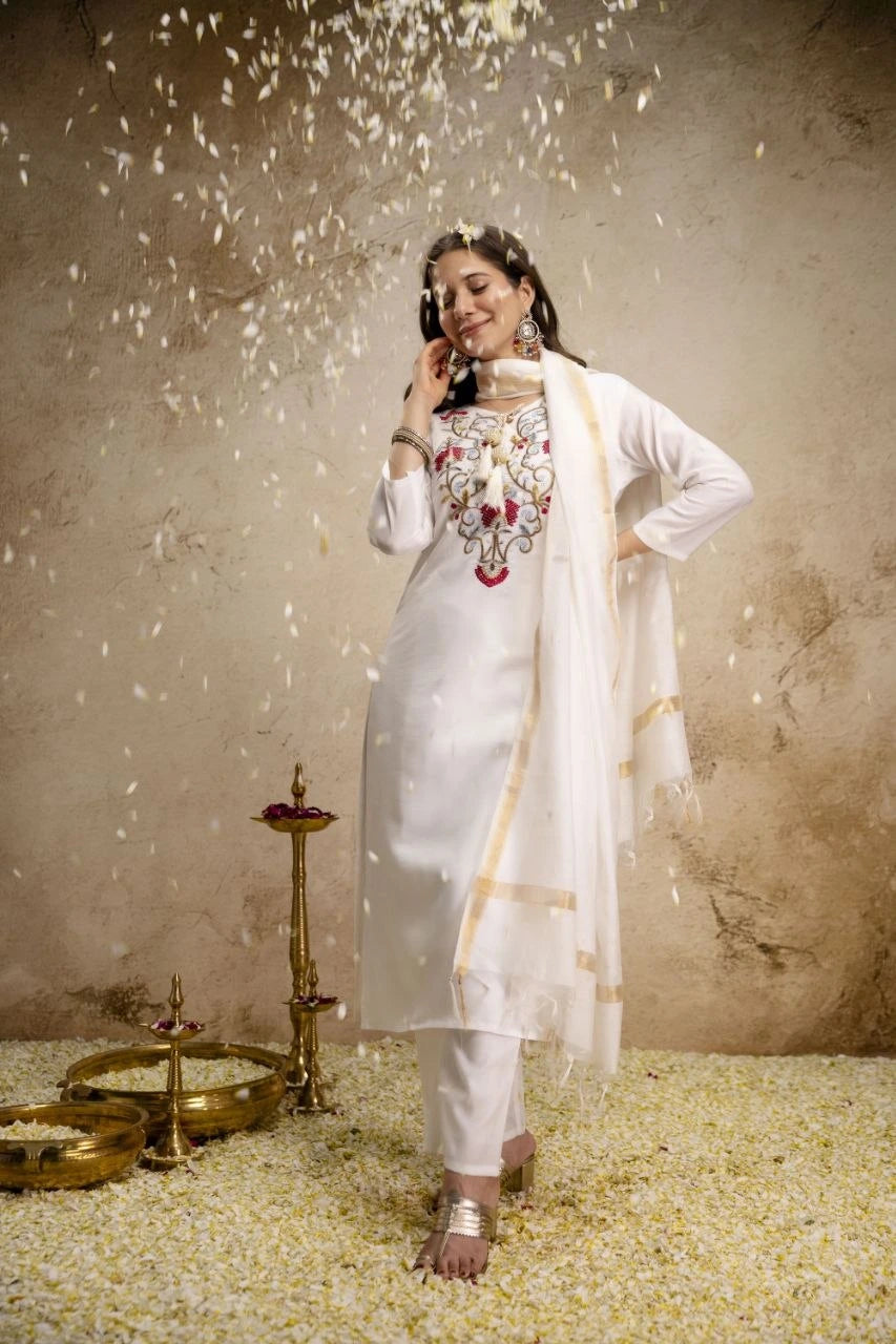 Woman in traditional outfit with floral design, standing against a textured wall with decorative elements.