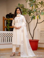 Woman in a white embroidered outfit standing indoors with plants in the background