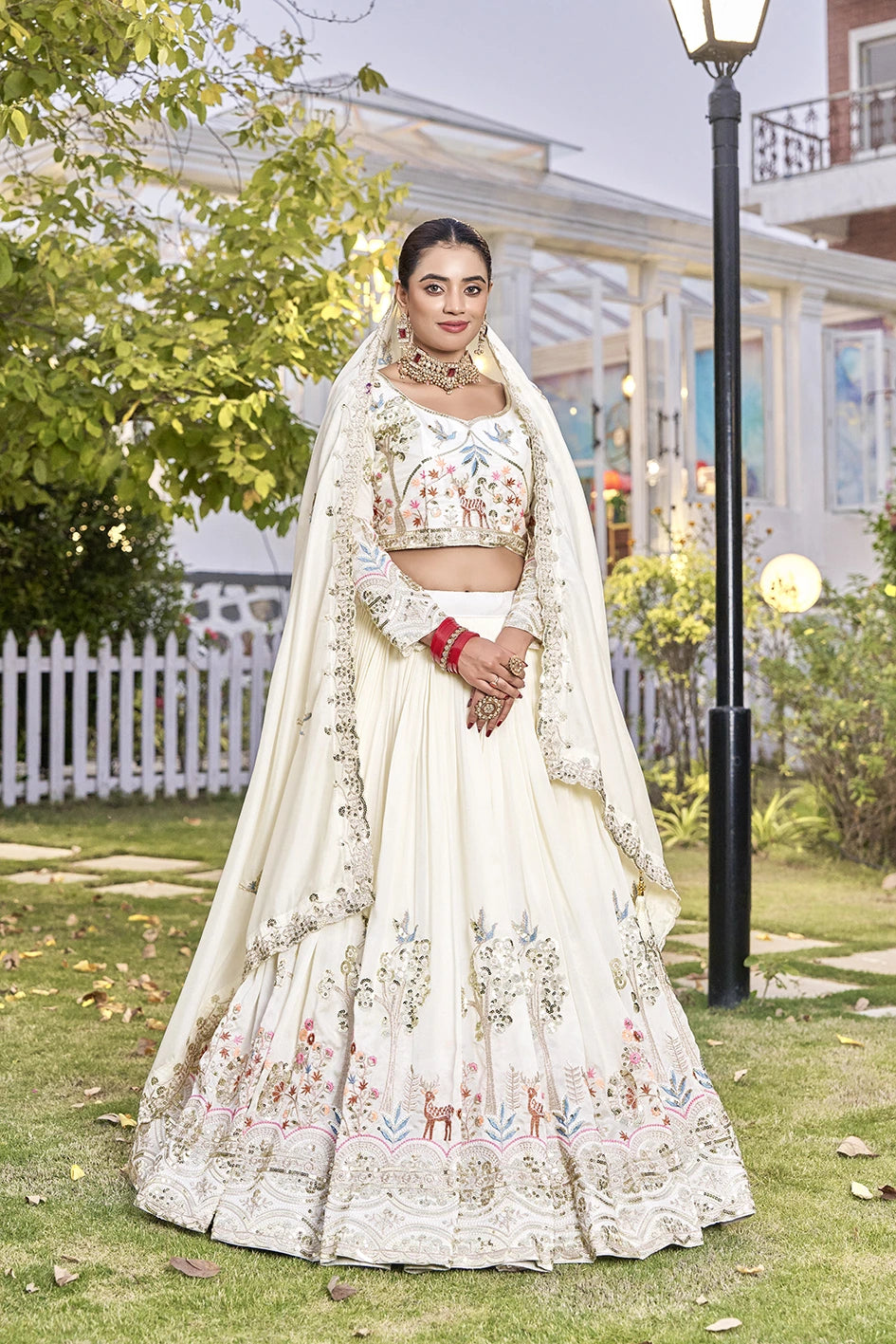 Woman in a traditional embroidered outfit standing outdoors with greenery and a building in the background