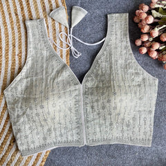 Light gray lace vest on a textured surface with flowers and a striped fabric.