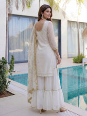 Woman in a white traditional outfit standing by a poolside.